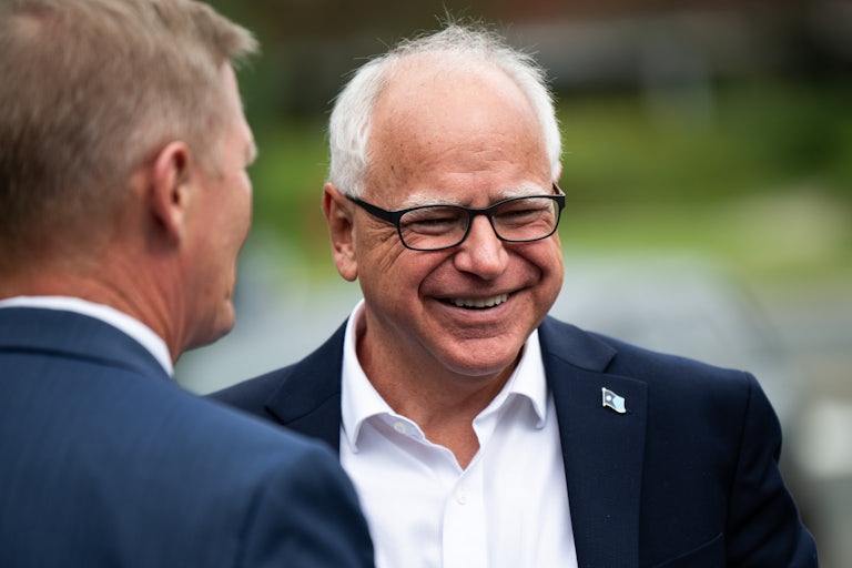 Minnesota Governor Tim Walz smiles broadly. Another man stands nearby.
