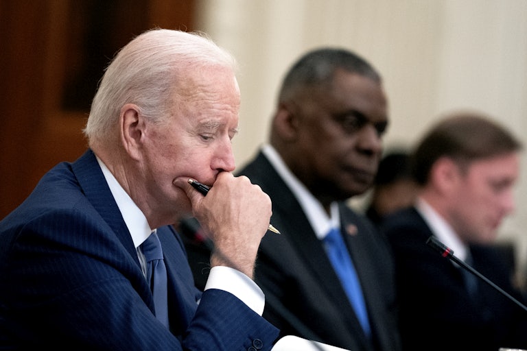 President Biden sits at a table with a pen and his chin in his hand.