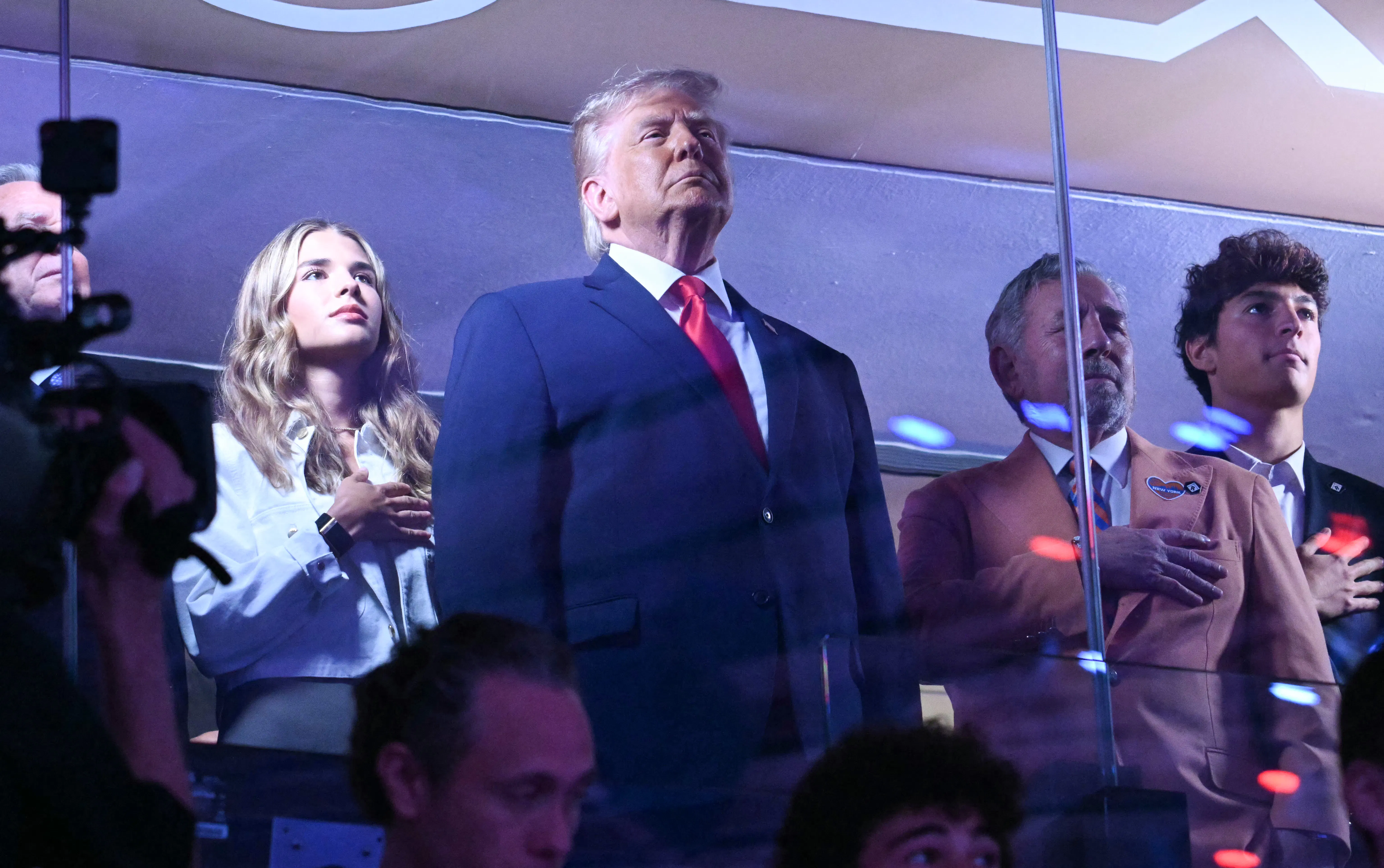 President Donald Trump stands as his granddaughter Kai Trump and Knicks owner James Dolan place their hands over their hearts.