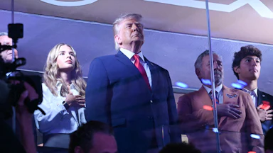 President Donald Trump stands as his granddaughter Kai Trump and Knicks owner James Dolan place their hands over their hearts.