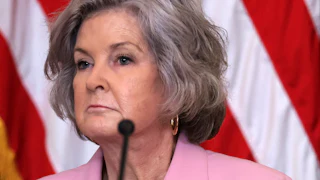 White House Chief of Staff Susie Wiles frowns while sitting in front of a microphone