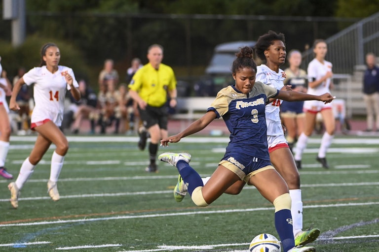Girls’ soccer teams on the field. One is about to kick a soccer ball.