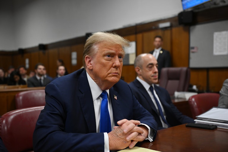 Donald Trump sits at a table with his hands folded
