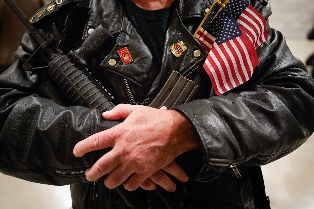 A man stands in the rotunda of the State Capitol holding a semi-automatic rifle.