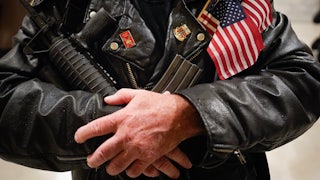A man stands in the rotunda of the State Capitol holding a semi-automatic rifle.