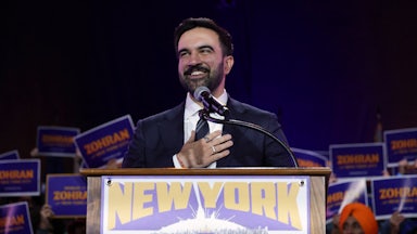 NYC Democratic mayoral moniee Zohran Mamdani stands at a lectern that reads "New York City is not for sale" as people hold Zohran signs behind him.