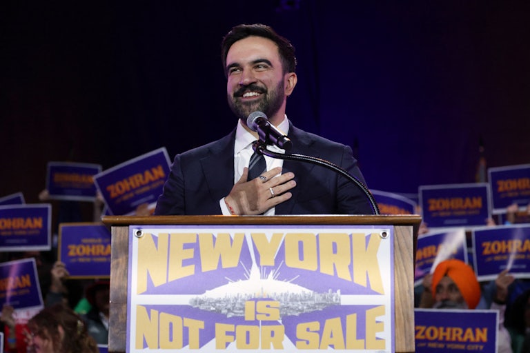 NYC Democratic mayoral moniee Zohran Mamdani stands at a lectern that reads "New York City is not for sale" as people hold Zohran signs behind him.