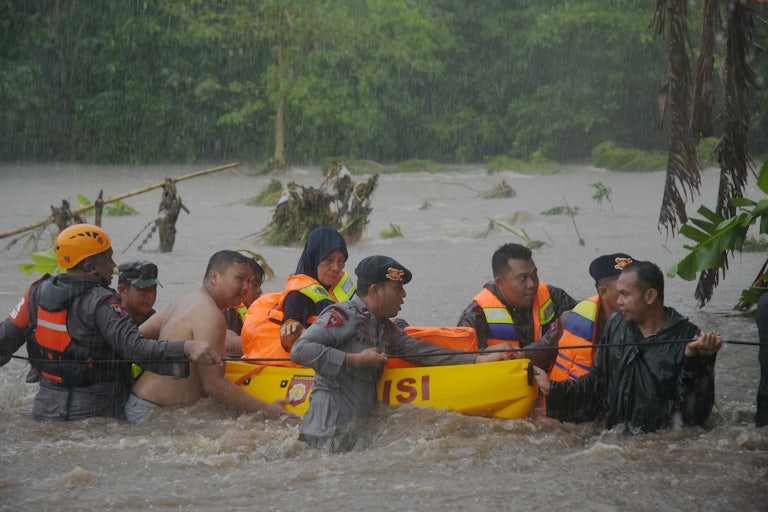Rescuers stand waist-deep in water, pulling a float through heavy rain.