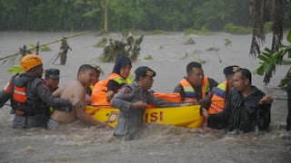 Rescuers stand waist-deep in water, pulling a float through heavy rain.