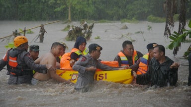Rescuers stand waist-deep in water, pulling a float through heavy rain.