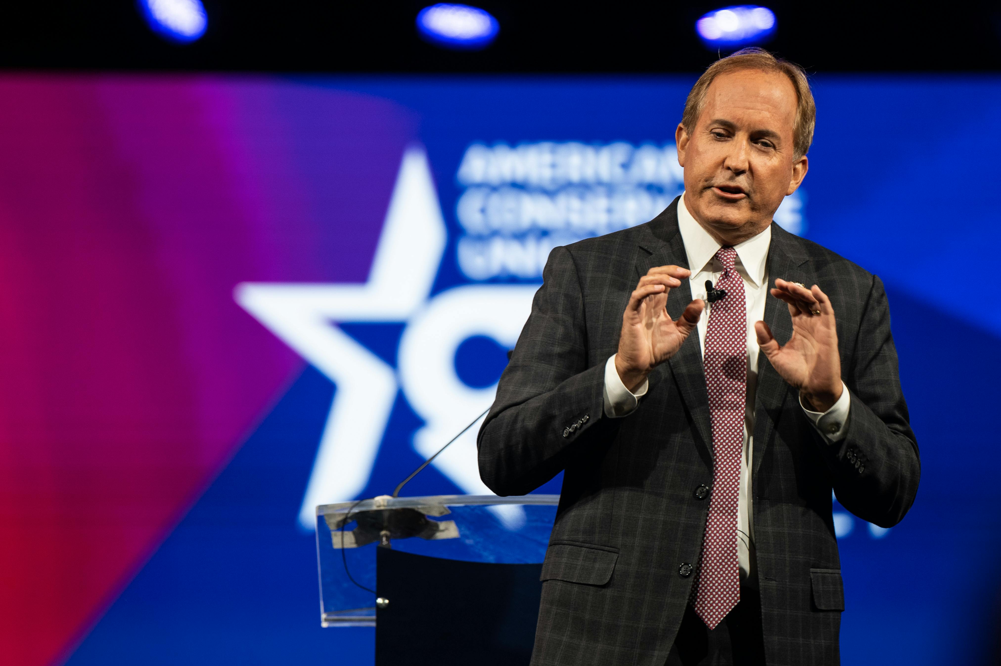 Texas Attorney General Ken Paxton speaks on stage in front of a Conservative Political Action Conference (CPAC) backdrop.