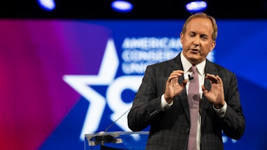 Texas Attorney General Ken Paxton speaks on stage in front of a Conservative Political Action Conference (CPAC) backdrop.