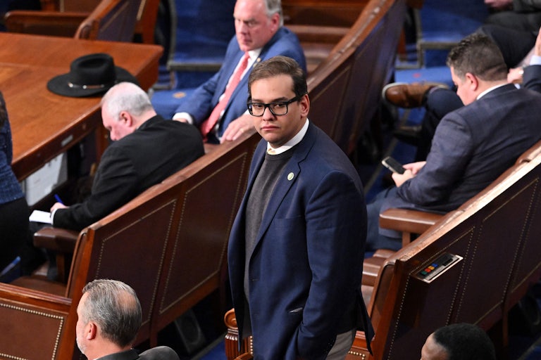 New York Representative George Santos stands in the House chamber while other congressman around him remain seated