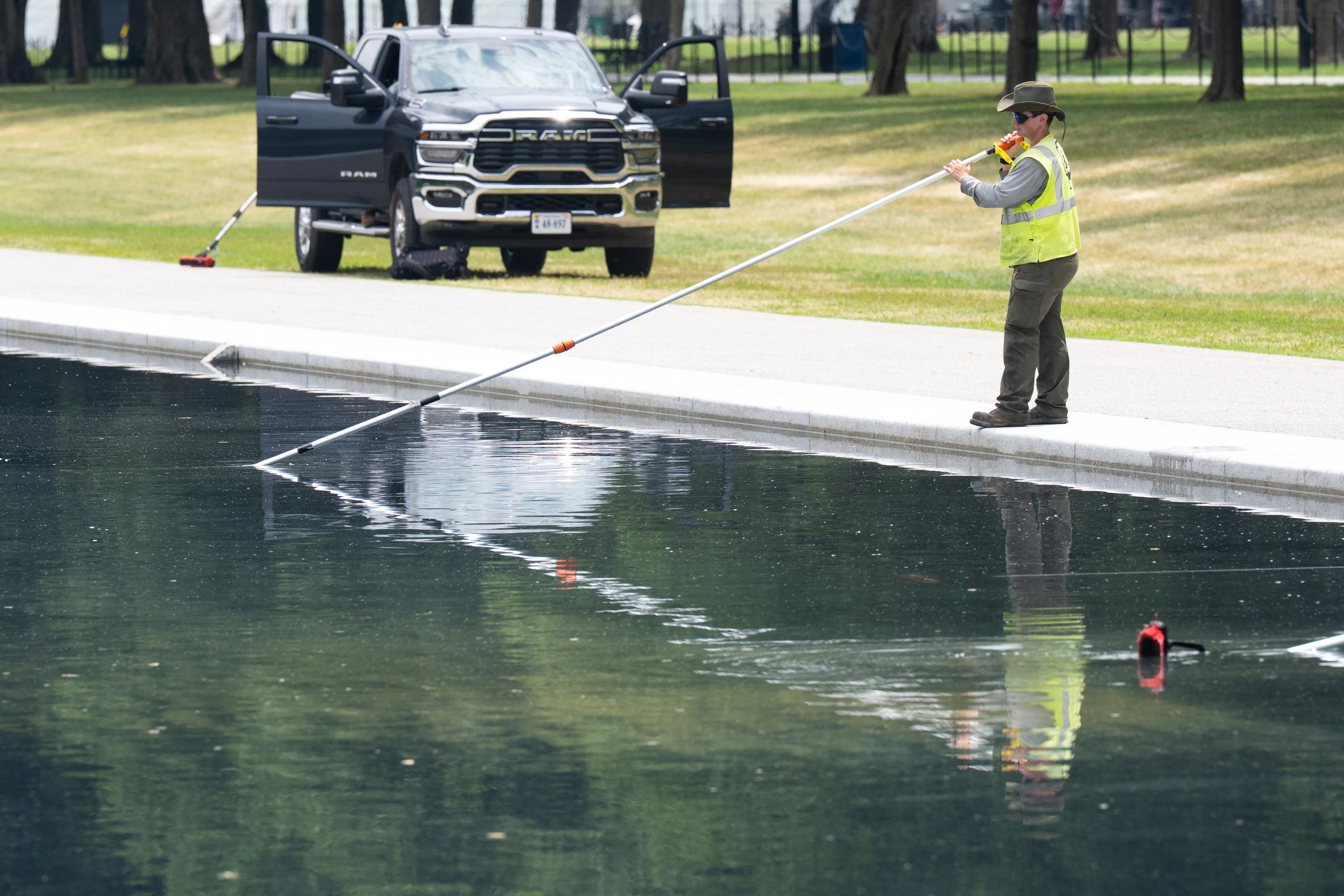 A worker uses a long-handled net to clean the Reflecting Pool