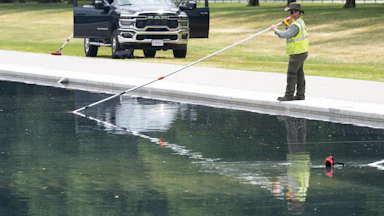 A worker uses a long-handled net to clean the Reflecting Pool