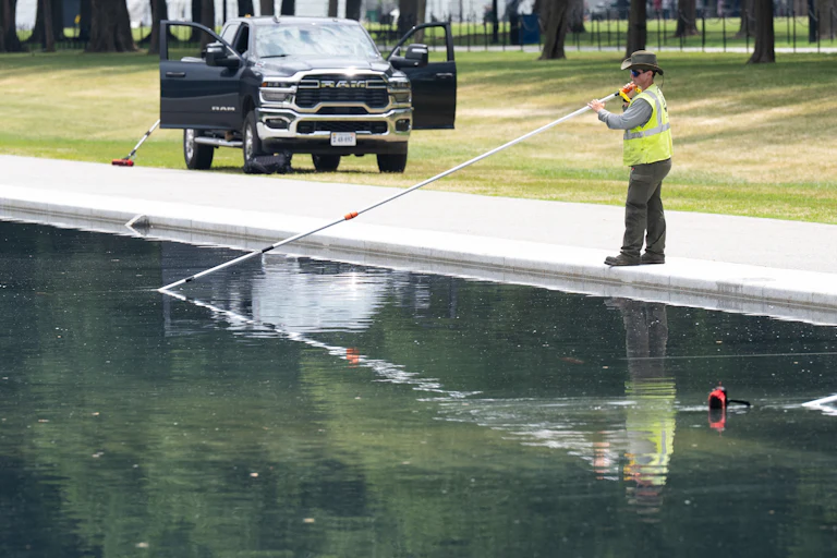 A worker uses a long-handled net to clean the Reflecting Pool