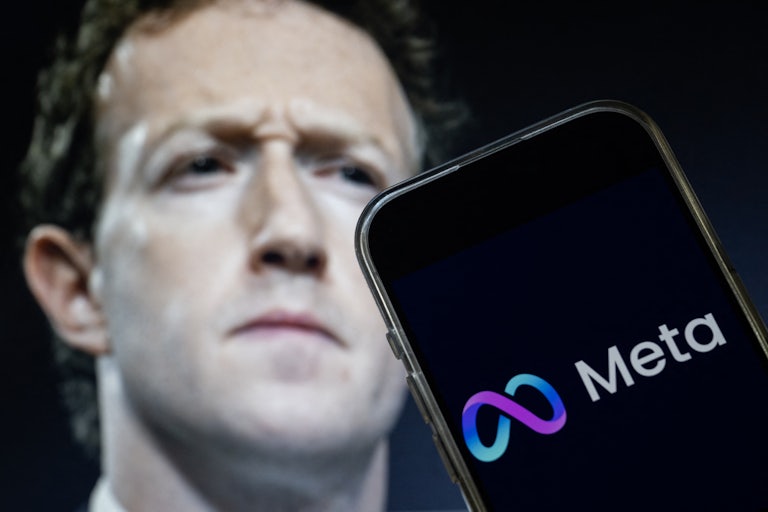 A photo of Mark Zuckerberg is seen behind a phone screen displaying Meta’s logo