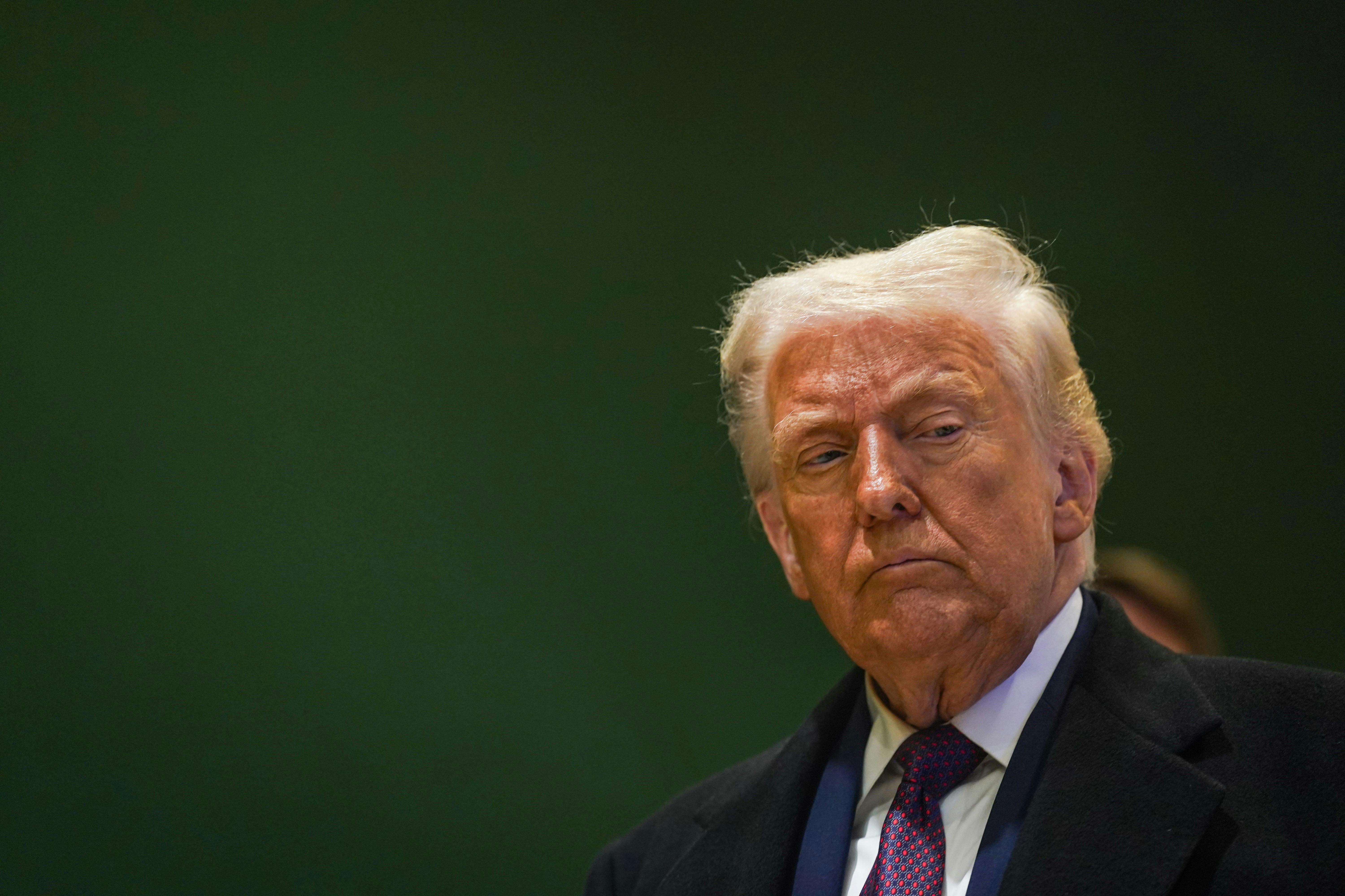 Donald Trump looks off while standing in front of a green backdrop.