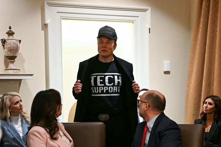 Elon Musk holds open his jacket to reveal the words "Tech Support" printed on his T-shirt, during Donald Trump's cabinet meeting