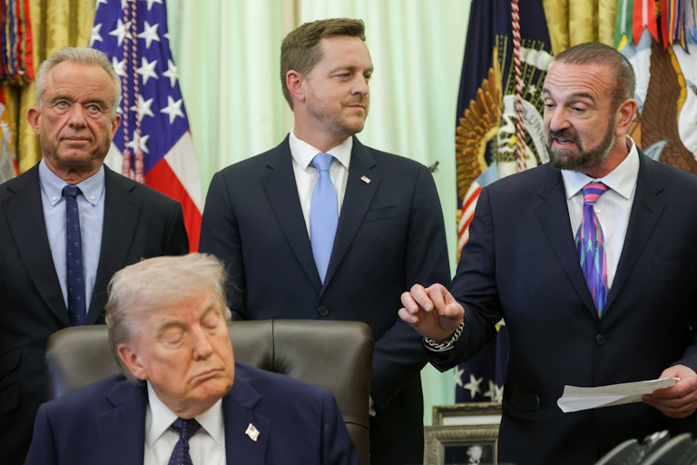 President and Chief Scientific Officer of Regeneron Pharmaceuticals George Yancopoulos speaks alongside Health Secretary Robert F. Kennedy Jr., Director of the Center for Medicare Chris Klomp, and Donald Trump during a White House event on health care affordability in the Oval Office. Trump's eyes are closed.