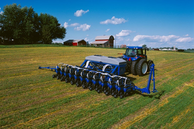A blue tractor drives over a field with a red barn in the background.