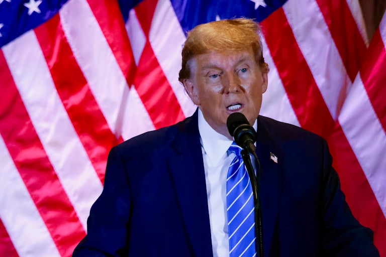Donald Trump speaks at a mic, with a U.S. flag behind him
