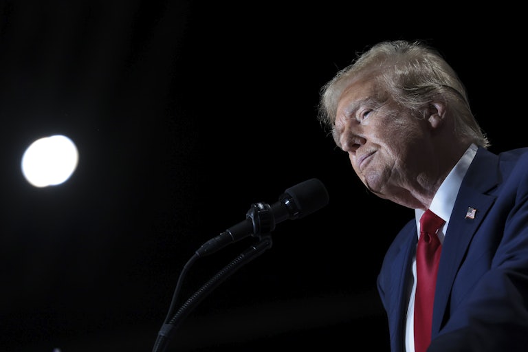 Donald Trump stands before a podium mic, profile shot