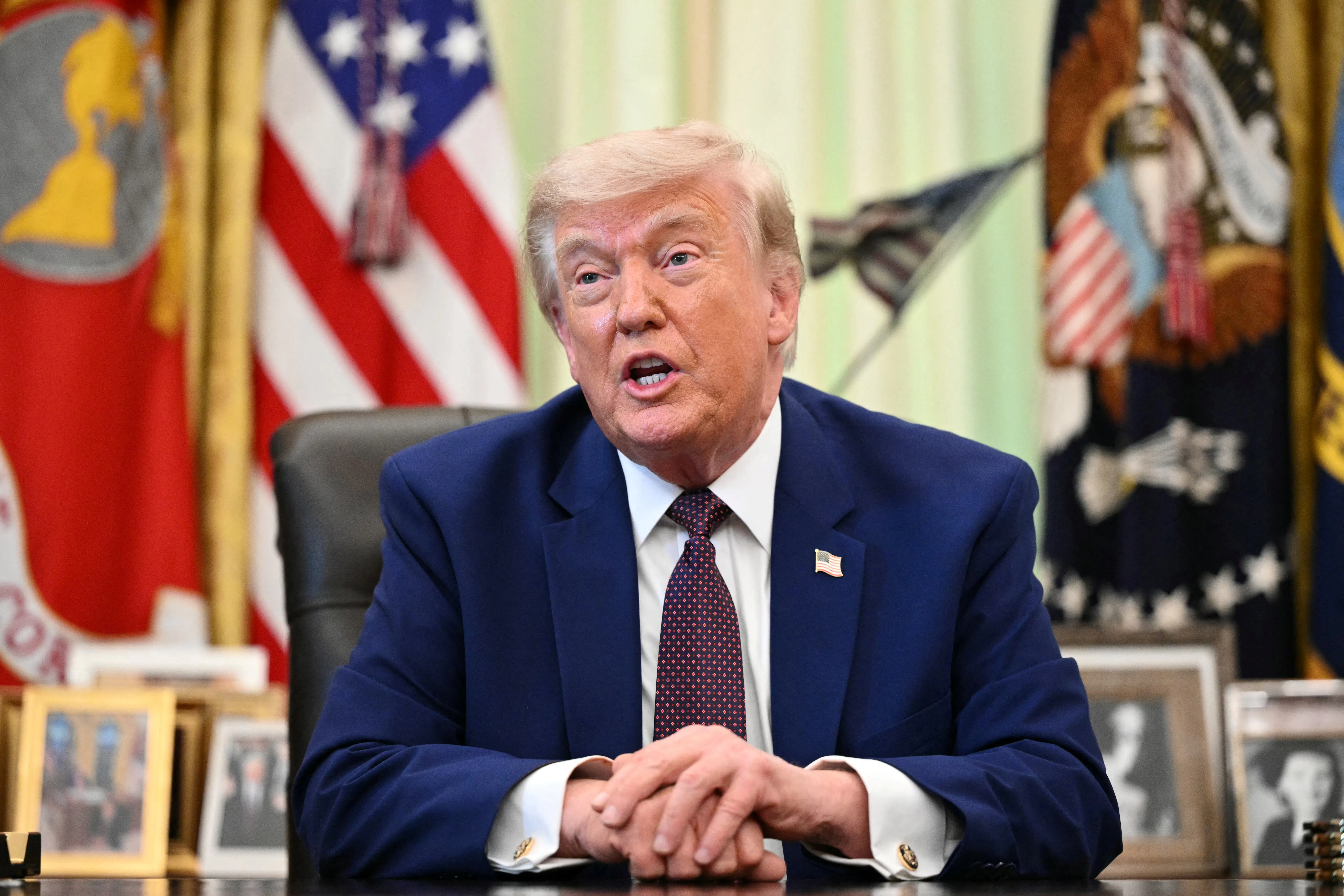 Donald Trump speaks while seated at his desk in the Oval Office of the White House