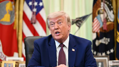 Donald Trump speaks while seated at his desk in the Oval Office of the White House