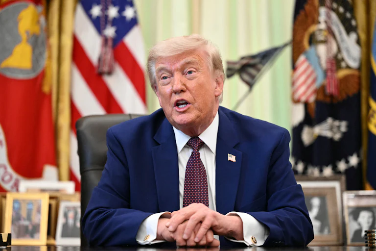 Donald Trump speaks while seated at his desk in the Oval Office of the White House