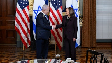 Benjamin Netanyahu and Kamala Harris shake hands while standing on front of Israeli and U.S. flags.