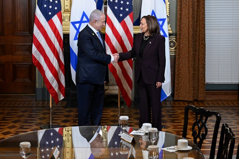 Benjamin Netanyahu and Kamala Harris shake hands while standing on front of Israeli and U.S. flags.