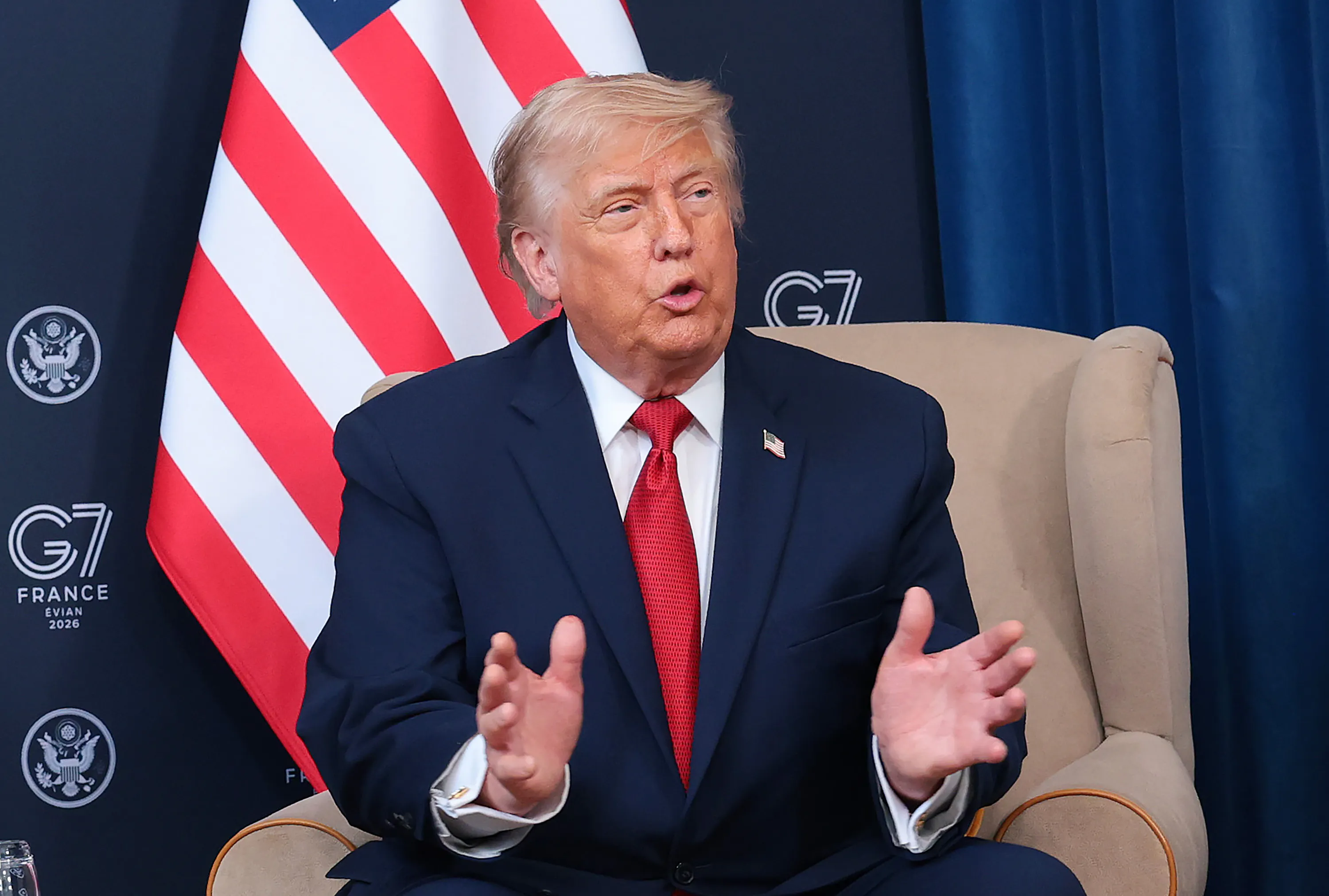 Donald Trump gestures and speaks while sitting in a press conference at the G7 summit