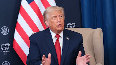 Donald Trump gestures and speaks while sitting in a press conference at the G7 summit