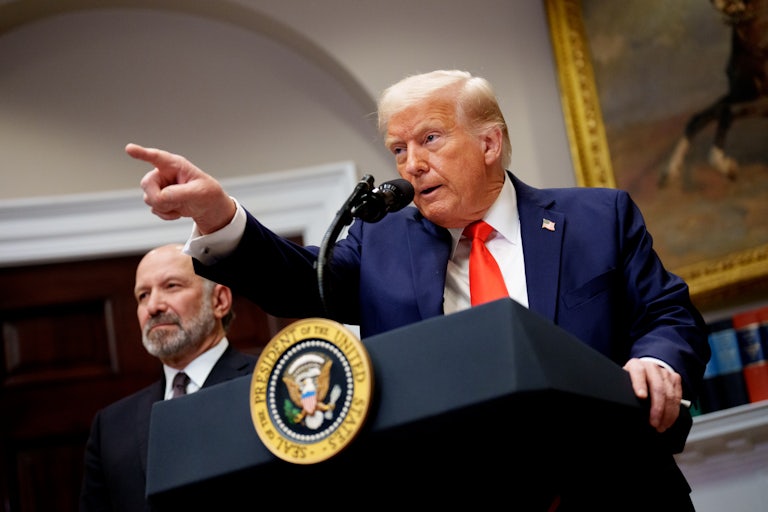 Donald Trump points at the presidential podium in the White House, while Commerce Secretary Harry Lutnick stands beside him.