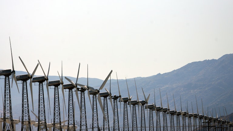 A row of wind turbines with hills in the background
