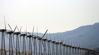 A row of wind turbines with hills in the background