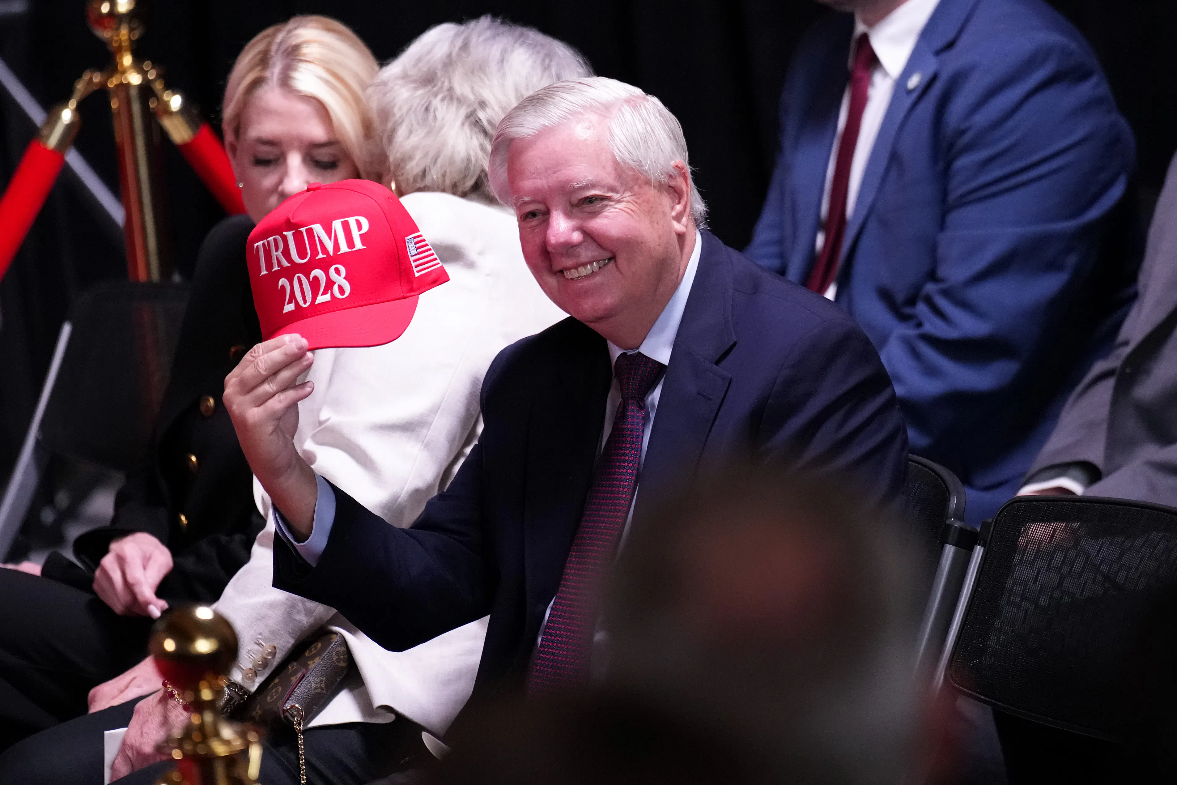 Lindsey Graham holds up a hat that reads "Trump 2028" during an event at the Kennedy Center. And now he's dead.