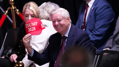 Lindsey Graham holds up a hat that reads "Trump 2028" during an event at the Kennedy Center. And now he's dead.
