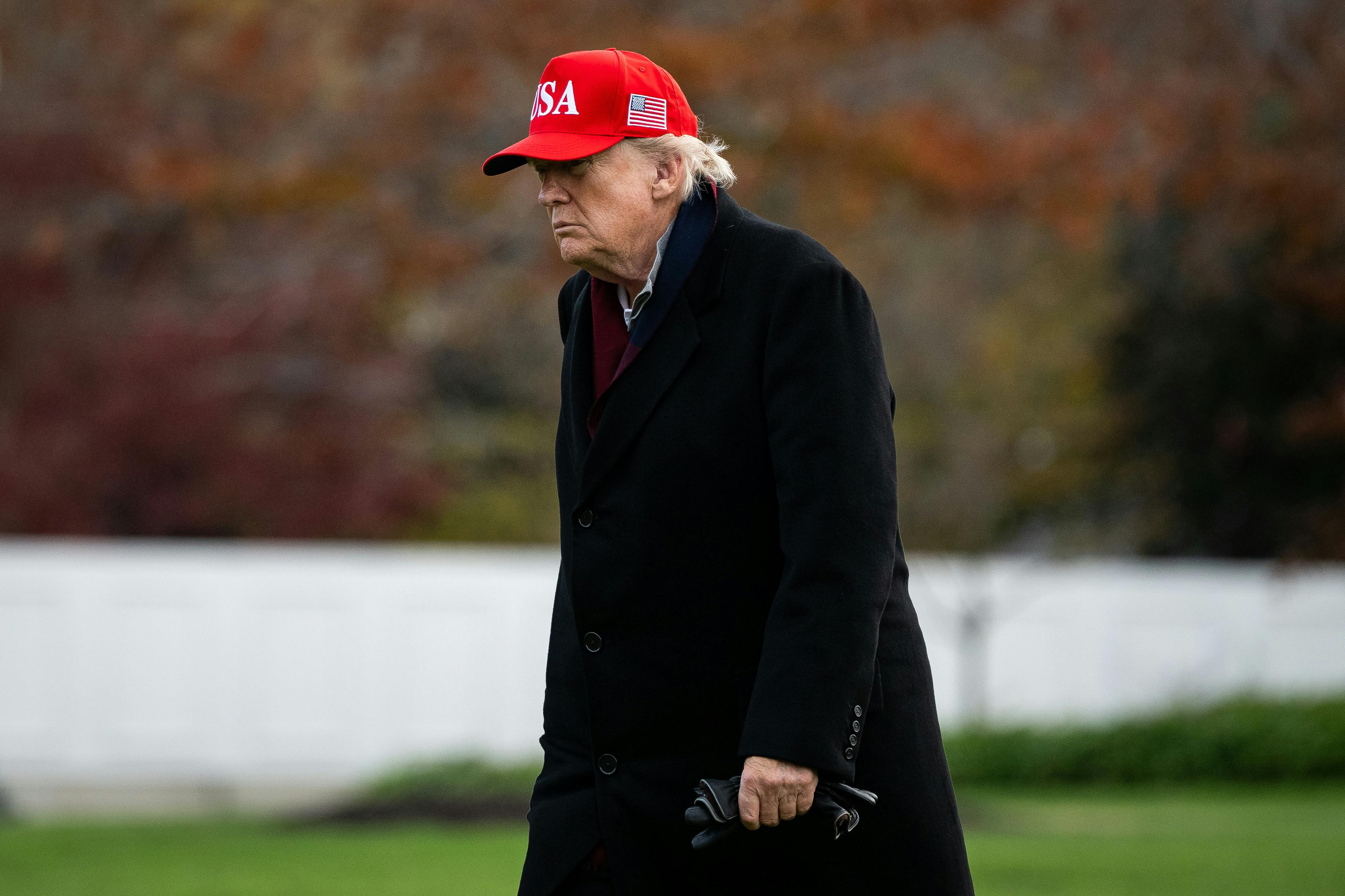 Donald Trump, wearing MAGA cap, walks with a stoop