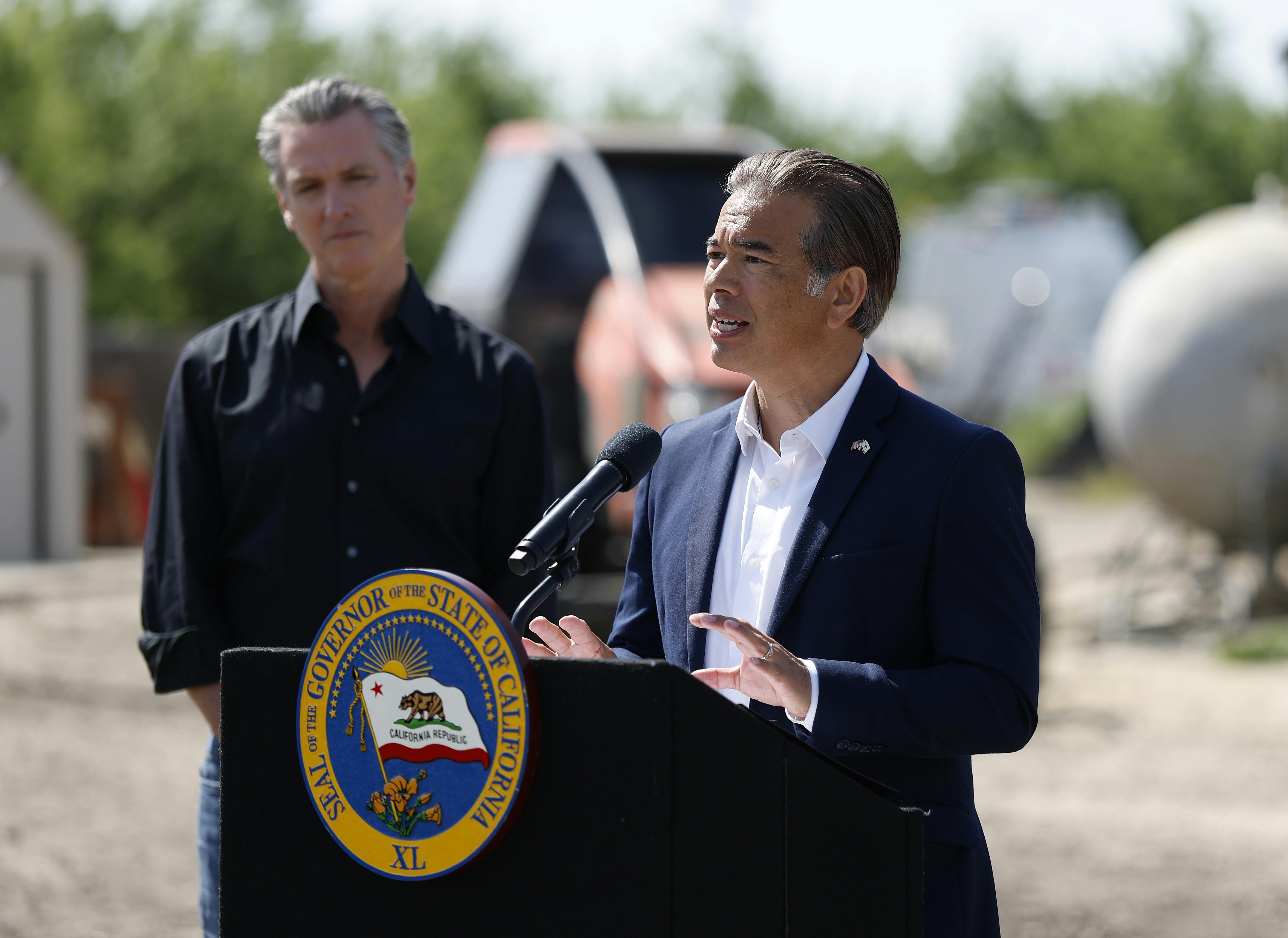 California Governor Gavin Newsom listens as state Attorney General Rob Bonta speaks at a podium with the state seal.