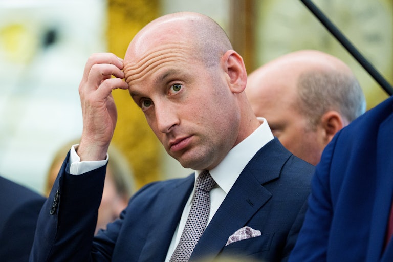 Stephen Miller scratches his forehead while standing in the Oval Office
