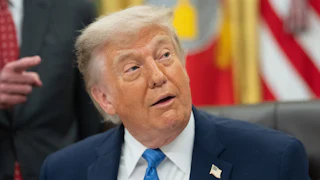 Donald Trump looks to the side while sitting at his desk in the Oval Office