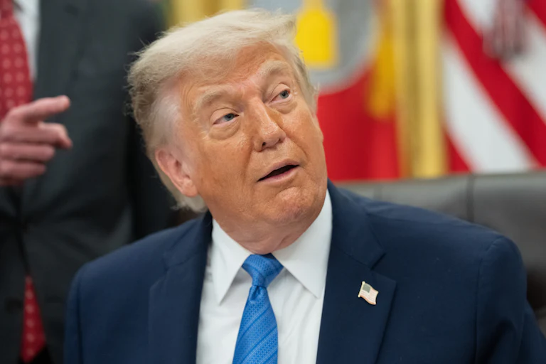 Donald Trump looks to the side while sitting at his desk in the Oval Office