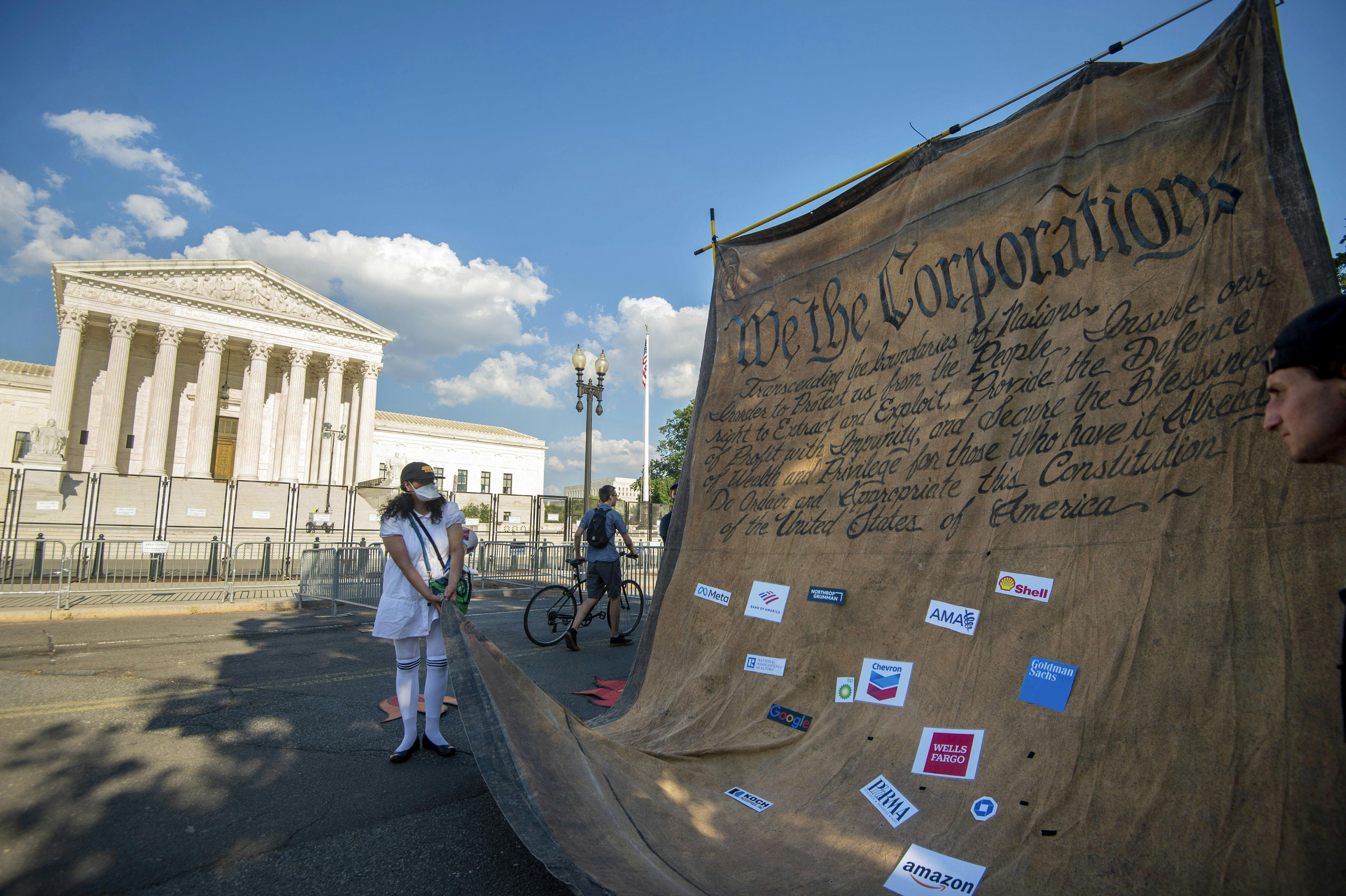Climate activists carry a giant model of the constitution, altered to say "We The Corporations," in front of the Supreme Court building in Washington, D.C.