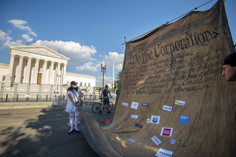 Climate activists carry a giant model of the constitution, altered to say "We The Corporations," in front of the Supreme Court building in Washington, D.C.
