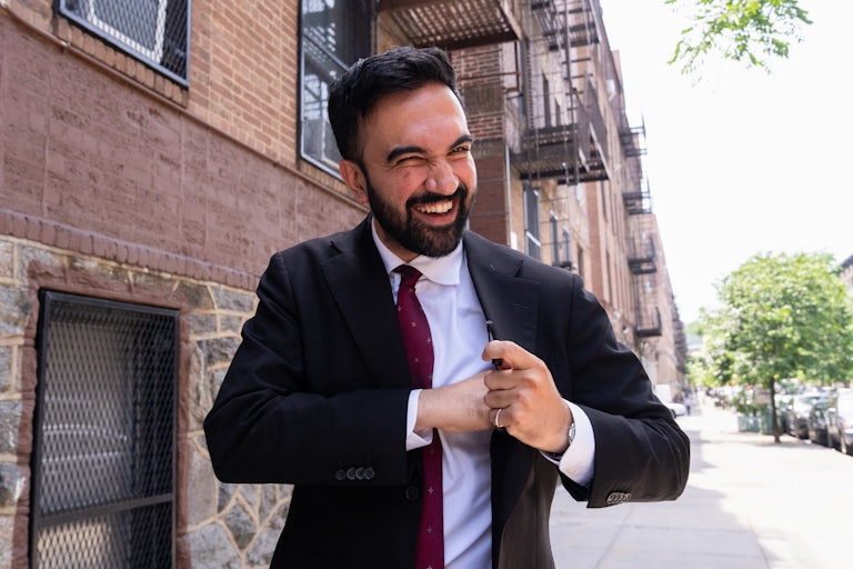 New York mayoral candidate Zohran Mamdani smiles and reaches into his jacket while walking in New York City