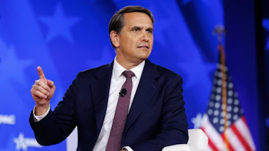 Deputy Attorney General Todd Blanche points a finger while seated in a chair on the CPAC stage.