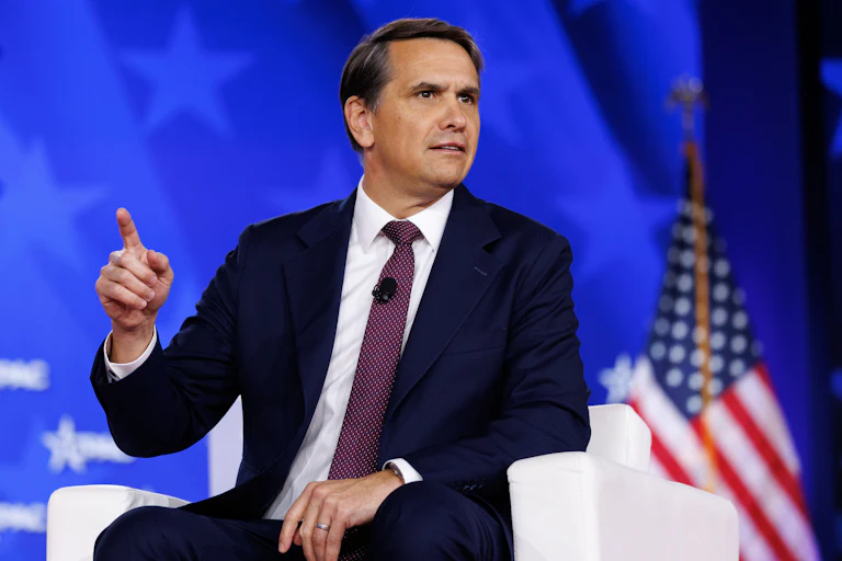 Deputy Attorney General Todd Blanche points a finger while seated in a chair on the CPAC stage.