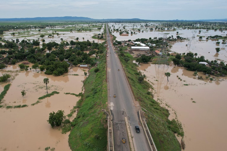 An aerial shot shows a raised road surrounded by floodwaters.